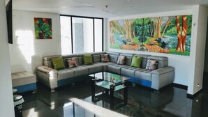 A modern living room with a sectional sofa, a glass coffee table, and a large forest-themed painting on the wall. - Hotel Basan Plaza (San Juan de Pasto)