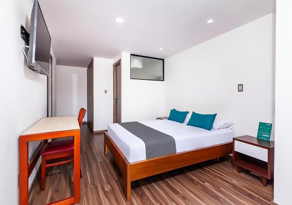 Une chambre d’hôtel avec un lit en bois, un bureau, une chaise et un téléviseur fixé au mur.