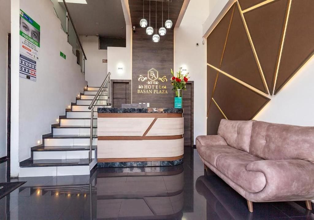 A hotel reception area with a modern design, including a reception desk, a staircase, and a sofa.