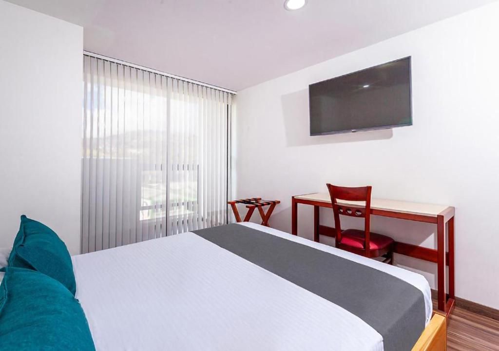 A hotel room with a bed, a desk, a chair, and a television on the wall.