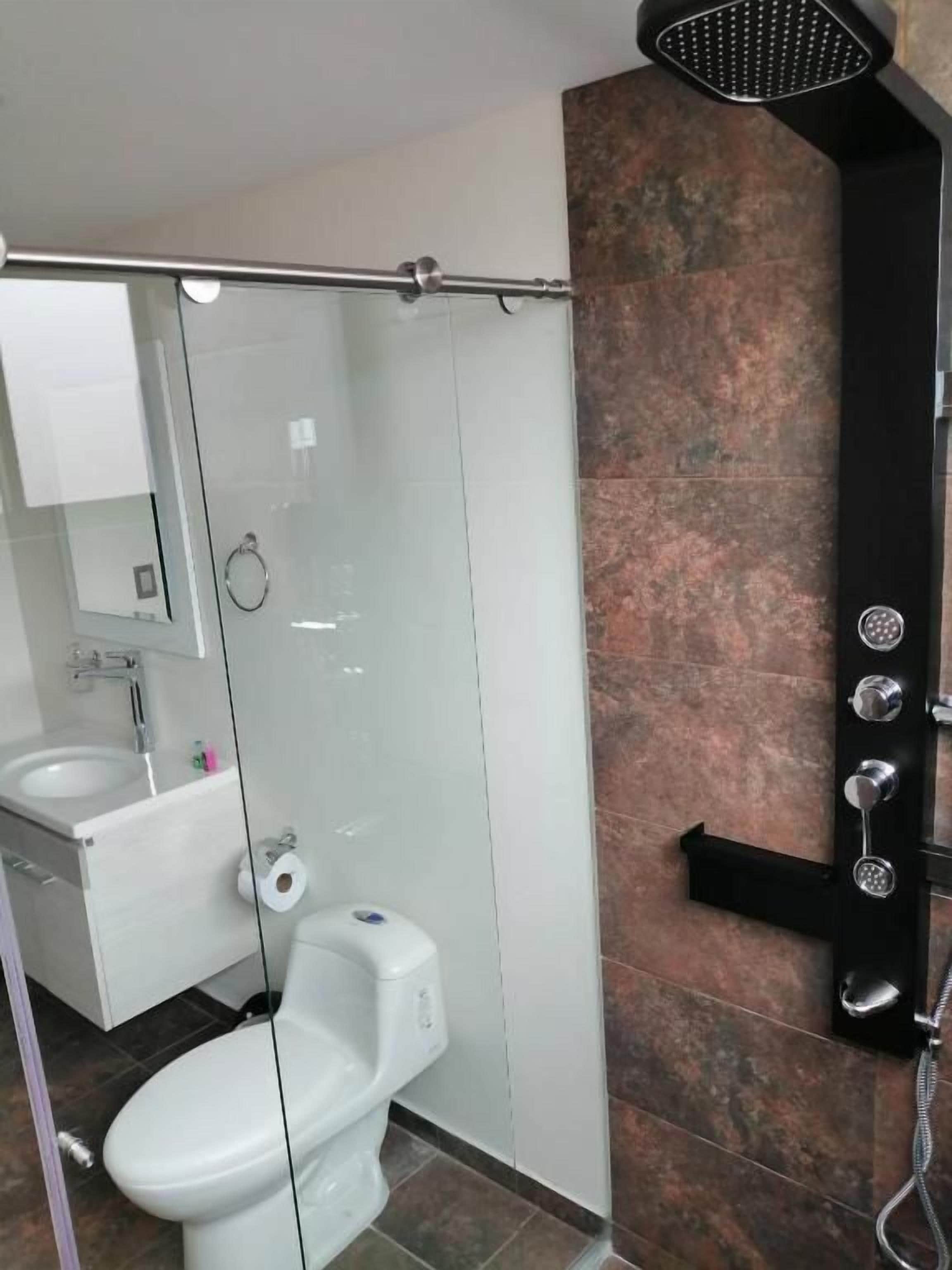 Un baño moderno con cabina de ducha de vidrio, un inodoro blanco y un perchero negro.
