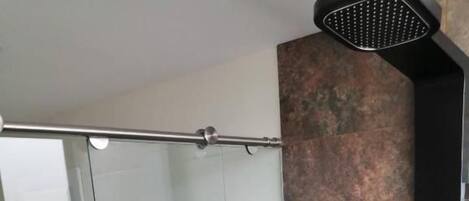 Un baño moderno con cabina de ducha de vidrio, un inodoro blanco y un perchero negro.