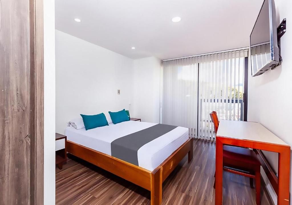 A hotel room with a wooden bed, a desk, and a TV mounted on the wall.