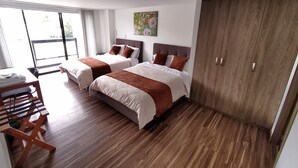 A hotel room with two beds, a wooden wardrobe, a desk with a chair, and a large window. - Hotel Basan Plaza (San Juan de Pasto)