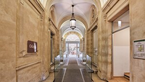 A grand hallway with classical architecture, including columns and arches, leading to a glass door entrance.