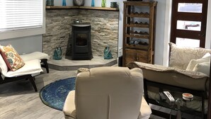A living room with a stone fireplace, a ceiling fan, a TV mounted on the wall, and a seating area with a sofa and armchairs. - Beautiful serene cottage (Fort Bragg)