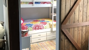 A bunk bed with colorful bedding, a wooden door, and a small desk with drawers. - Beautiful serene cottage (Fort Bragg)