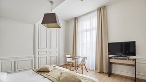 A hotel room with a bed, a desk, a chair, a television, and a window with curtains. - Wi-Fi + Climatisation ! Studio spacieux au Centre (Montpellier)