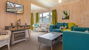A cozy living room with a television mounted on the wall, a sofa, a coffee table, and a wicker chair.