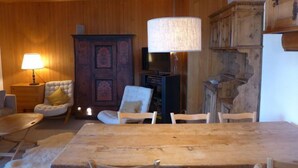 A wooden dining table with chairs, a television, and a cabinet in a room with wooden walls and a hanging lamp. - Montagnards 17 by Interhome (Villars)