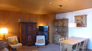 A cozy room with a wooden ceiling, a television, a cabinet, a dining table with chairs, and a lamp. - Montagnards 17 by Interhome (Villars)