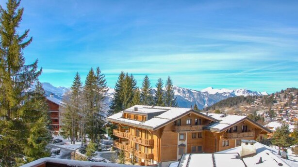 A wooden chalet with a balcony, surrounded by snow-covered trees and mountains in the background. - Montagnards 17 by Interhome (Villars)