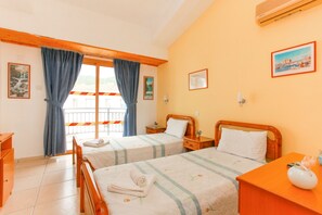 A hotel room with two beds, wooden headboards, a wooden dresser, a nightstand, a window with curtains, and a wall-mounted air conditioner.