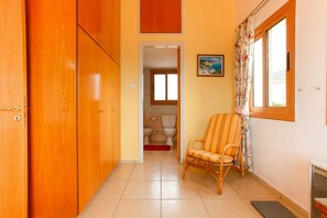 A hallway with wooden doors, a wicker chair, a painting, and a window with curtains.