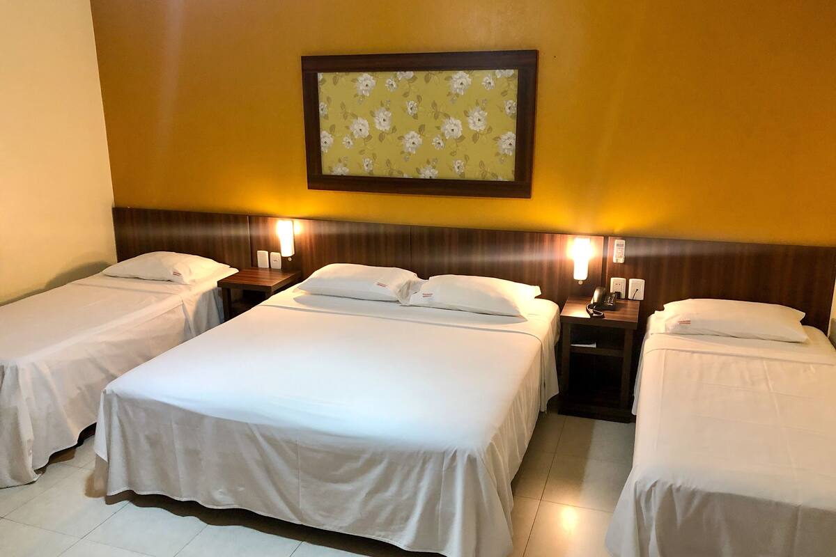 Habitación de hotel con una cama grande, dos mesitas de noche y un televisor montado en la pared.