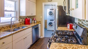 A kitchen with a granite countertop, stainless steel sink, white cabinets, a built-in oven, and a washing machine in the adjacent room.