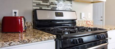 A kitchen with a gas stove, a red toaster, and a microwave.