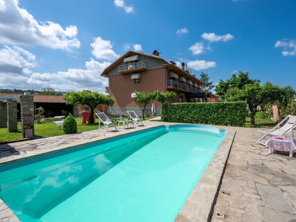 Ein Schwimmbecken mit Liegestühlen, ein Backsteinhaus mit Balkonen und ein gepflegter Garten.