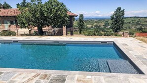 A rectangular swimming pool with stone tiles, surrounded by a patio area with a view of a rural landscape. - Beautiful  villa for 4 people with WIFI, private pool, TV, terrace and panoramic view (Castagnole Delle Lanze)