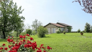 Una casa con tetto in tegole rosse, circondata da un prato curato e cespugli fioriti.