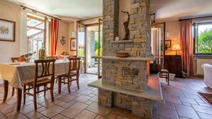 A dining area with a stone fireplace, wooden chairs, a table with a white tablecloth, and a view of the outdoors through large windows. - Wonderful  villa for 8 guests with private pool, A/C, WIFI, hot tub, TV and terrace (Narzole)