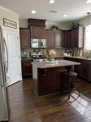 A kitchen with dark wooden cabinets, a stainless steel oven, a granite countertop, and a central island with stools.