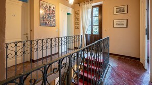 Una escalera con barandales de metal decorativos, un rellano alfombrado de rojo y un candelabro en el techo.