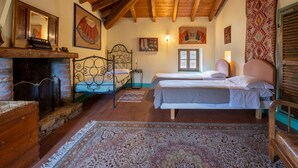 Un dormitorio abrigado en el ático con techo de madera, chimenea, dos camas y una ventana.