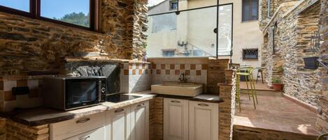 Una cocina rústica con paredes de piedra, techo de madera y vista a un edificio cercano.