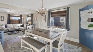 A dining area with a wooden table and chairs, a chandelier, and a view of the outside. - The Comfy Craftsman l KING Beds l Near Park l Spacious Home (Spokane)