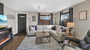 A modern living room with a sectional sofa, a coffee table, a fireplace, and a television. - The Comfy Craftsman l KING Beds l Near Park l Spacious Home (Spokane)