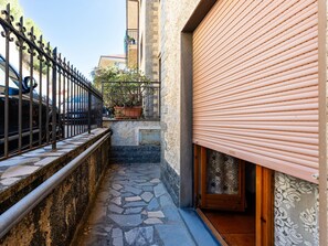 A narrow alleyway with a stone-paved path, a metal fence, and a potted plant.