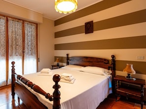 A hotel room with a wooden bed, two bedside tables, a lamp, and a window with curtains.