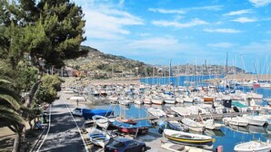 A marina with numerous boats docked, a road with parked cars, and a hilly landscape in the background. - Cosy apartment for 3 people with WIFI, TV, balcony and pets allowed (Vallecrosia)