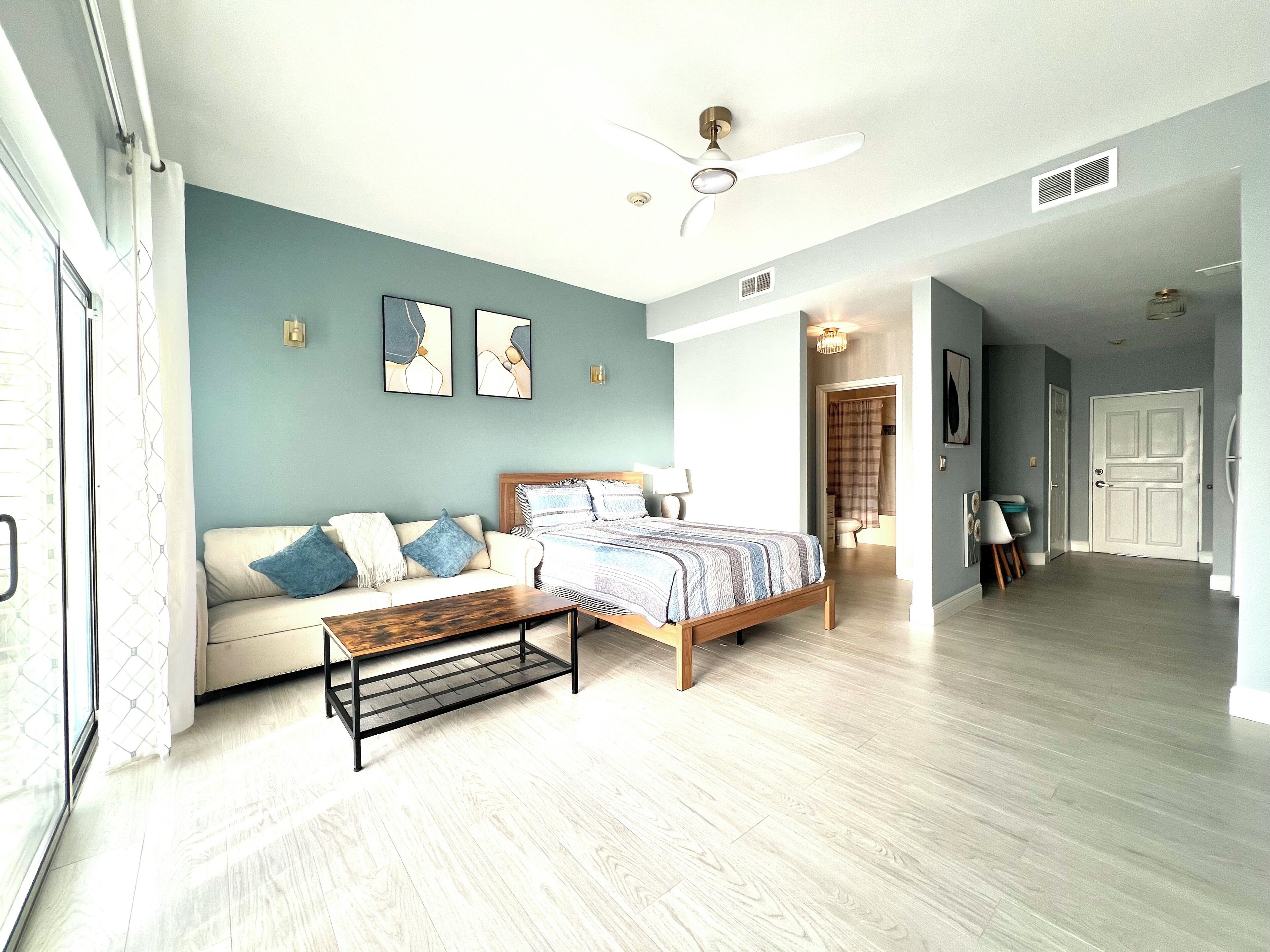 A bedroom with a bed, a sofa, a coffee table, and a ceiling fan.