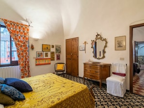 Um quarto com uma cama, cômoda, cadeira, espelho e obras de arte nas paredes.