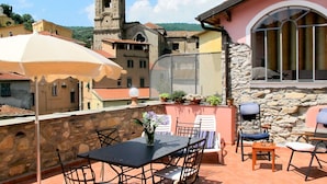 A terrace with a table and chairs, a stone wall, and a view of a church tower. - Lovely apartment for 4 people with terrace (Dolcedo)
