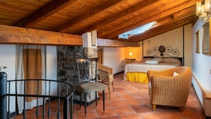 A cozy attic bedroom with a stone wall, wooden beams, a bed with a headboard, a wicker chair, and a small table. - Lovely apartment for 4 people with terrace (Dolcedo)