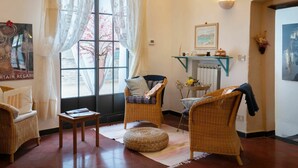 A cozy living room with wicker furniture, a large window with sheer curtains, a fireplace, and a clock on the wall. - Lovely apartment for 4 people with terrace (Dolcedo)