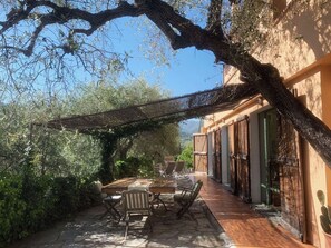 Une terrasse avec une table et des chaises, une pergola et un bâtiment doté de volets en bois.