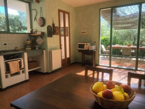 A kitchen with a dining table, a microwave, and a basket of fruit.