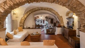 Une pièce chaleureuse avec une arche en pierre, un canapé, une petite table ronde et un coin cuisine visible à travers l’arche.
