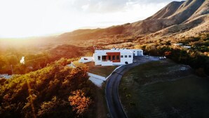 Un bâtiment moderne de couleur blanche, agrémenté d’une touche de rouge, entouré d’un paysage vallonné et bordé d’une route sinueuse.