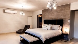 Une chambre à coucher moderne avec un grand lit, un banc, une chaise et une table de chevet avec une lampe.