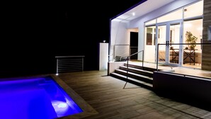 Une maison moderne dotée d’une piscine, d’un escalier menant à une porte en verre et d’un coin repas visible à travers le verre.