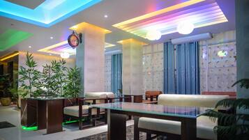 Um lobby moderno com áreas de estar, um relógio grande e iluminação decorativa.