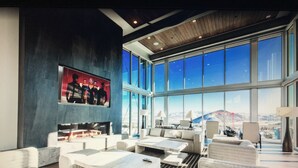 A spacious lounge with a large TV screen, comfortable seating, and a view of a mountainous landscape through large windows.
