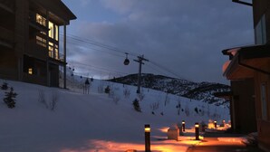 A snow-covered street with buildings on either side, a ski lift in the background, and a clear sky.