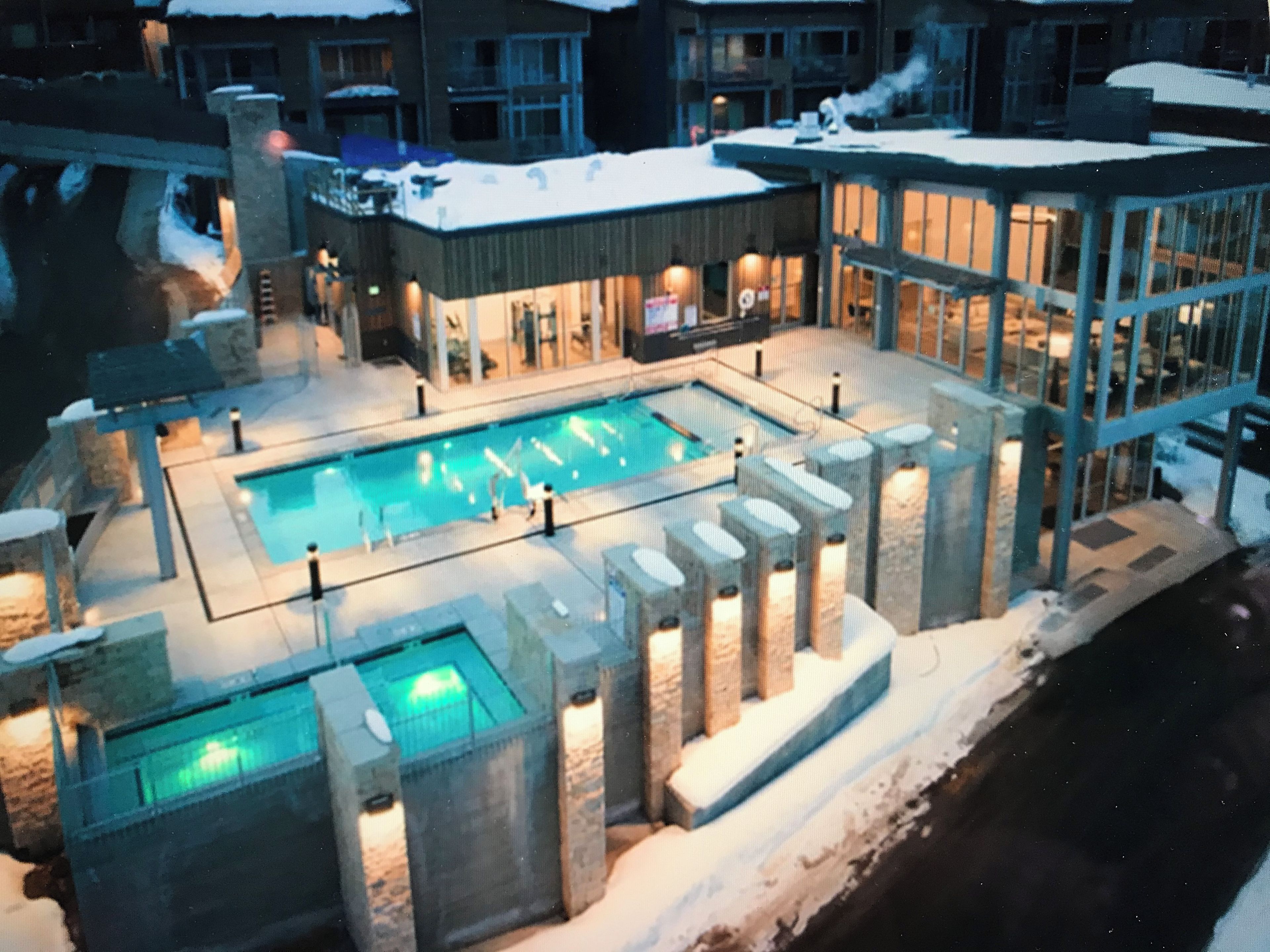 Ett poolområde med flera pooler, stenpelare och en byggnad med upplysta fönster.