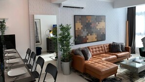 A modern living room with a sectional sofa, dining table, chairs, a large abstract painting, and a potted plant. - Santo Domingo Apartment with Rooftop Pool with Ocean & City Views (Santo Domingo)